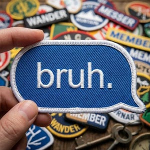May include: A blue patch in a speech bubble shape with the word "bruh." in white. The patch is held in a hand, with a collection of other patches in the background.