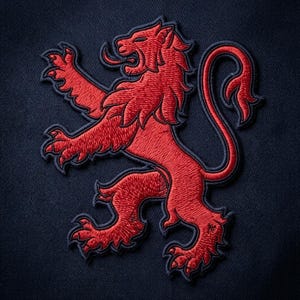 May include: A dark navy blue fabric background featuring a vibrant red embroidered lion patch. The lion is depicted in a rampant position, showing sharp claws, a flowing mane, and a curled tail, all outlined with a dark navy blue thread border.