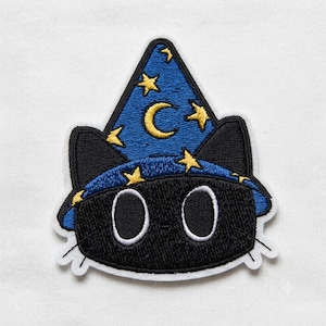 May include: An embroidered patch featuring a black cat head wearing a blue wizard hat. The hat is decorated with yellow stars and a yellow crescent moon. The cat has large white-outlined eyes and black whiskers, all bordered by a white edge.