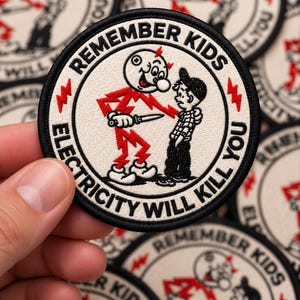 May include: A circular embroidered patch with a black border on a white background. It features a cartoon character made of red lightning bolts holding a knife toward a small boy. The text reads REMEMBER KIDS ELECTRICITY WILL KILL YOU.