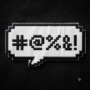 May include: A rectangular embroidered patch featuring a white speech bubble with a black pixelated border. Inside the bubble, black pixelated symbols representing profanity, specifically #@%&!, are embroidered against the white background.