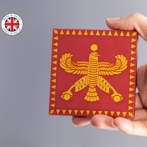 Könnte beinhalten: Ein roter quadratischer Untersetzer mit einem stilisierten gelben Vogeldesign. Der Untersetzer hat einen gelben Dreiecksrand. Der Aufkleber "MADE IN THE UK" befindet sich in der oberen linken Ecke.