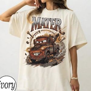 Puede incluir: Camiseta de color marfil con una imagen de dibujos animados de Mater de la pel&iacute;cula Cars. El gr&aacute;fico incluye la palabra "MATER" encima del personaje, con herramientas y un dise&ntilde;o de reloj en el fondo. La camiseta es de corte holgado.