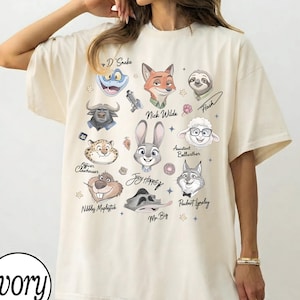 Może przedstawiać: Kremowa koszulka oversize z ilustracjami postaci z kresk&oacute;wek. Koszulka zawiera postacie takie jak Nick Wilde, Judy Hopps i Flash. Słowo "Ivory" jest wydrukowane w lewym dolnym rogu.