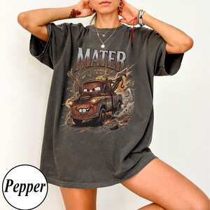 Puede incluir: Camiseta gris oscuro con una imagen de dibujos animados de Mate de la pel&iacute;cula Cars. La palabra "MATER" est&aacute; impresa encima de la imagen en un estilo desgastado. El gr&aacute;fico incluye rayos y un fondo desgastado.