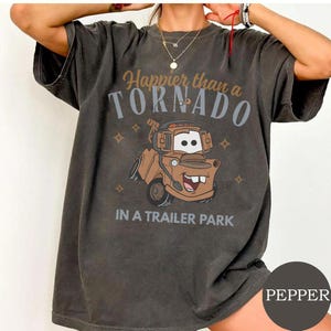 May include: Dark gray t-shirt featuring a cartoon image of a brown tow truck with the text "Happier than a Tornado in a Trailer Park." The shirt has a vintage, worn look.