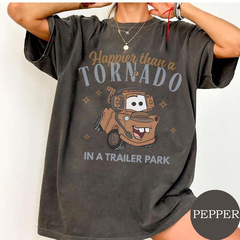 May include: Dark gray t-shirt featuring a cartoon image of a brown tow truck with the text "Happier than a Tornado in a Trailer Park." The shirt has a vintage, worn look.
