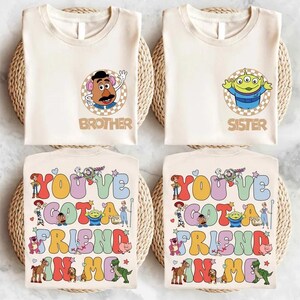 May include: Four cream-coloured t-shirts with Toy Story graphics. Two shirts feature Mr. Potato Head and an alien, with the words "Brother" and "Sister." The other two shirts display the phrase "You've Got a Friend in Me" with character illustrations.