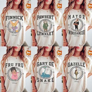 May include: Cream-colored t-shirts featuring characters from the Disney movie Zootopia. Each shirt displays a character's name in a circular design with the Disney logo. Characters include Finnick, Pawbert Lynxley, Mayor Winddancer, Fru Fru, Gary De Snake, and Gazelle.