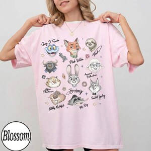 Może przedstawiać: Jasnor&oacute;żowa koszulka z portretami postaci z kresk&oacute;wek z filmu. Koszulka zawiera imiona "Gary D'Snake", "Nick Wilde", "Judy Hopps" i innych. Słowo "Blossom" jest wydrukowane w lewym dolnym rogu.