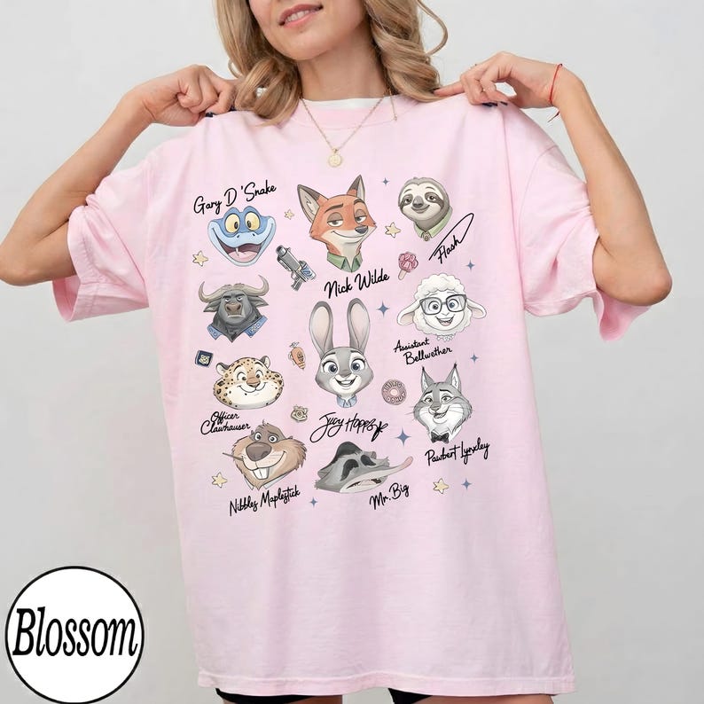 Może przedstawiać: Jasnor&oacute;żowa koszulka z portretami postaci z kresk&oacute;wek z filmu. Koszulka zawiera imiona "Gary D'Snake", "Nick Wilde", "Judy Hopps" i innych. Słowo "Blossom" jest wydrukowane w lewym dolnym rogu.