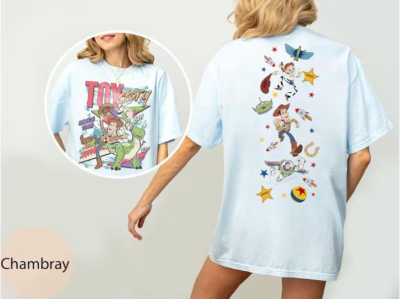 Puede incluir: Una camiseta azul claro con gr&aacute;ficos de Toy Story. El frente muestra a Woody y Rex con el texto "Toy Story". La parte posterior presenta una disposici&oacute;n vertical de personajes que incluye a Woody, Buzz Lightyear, un alien&iacute;gena y varios iconos como estrellas, cohetes y una pelota.