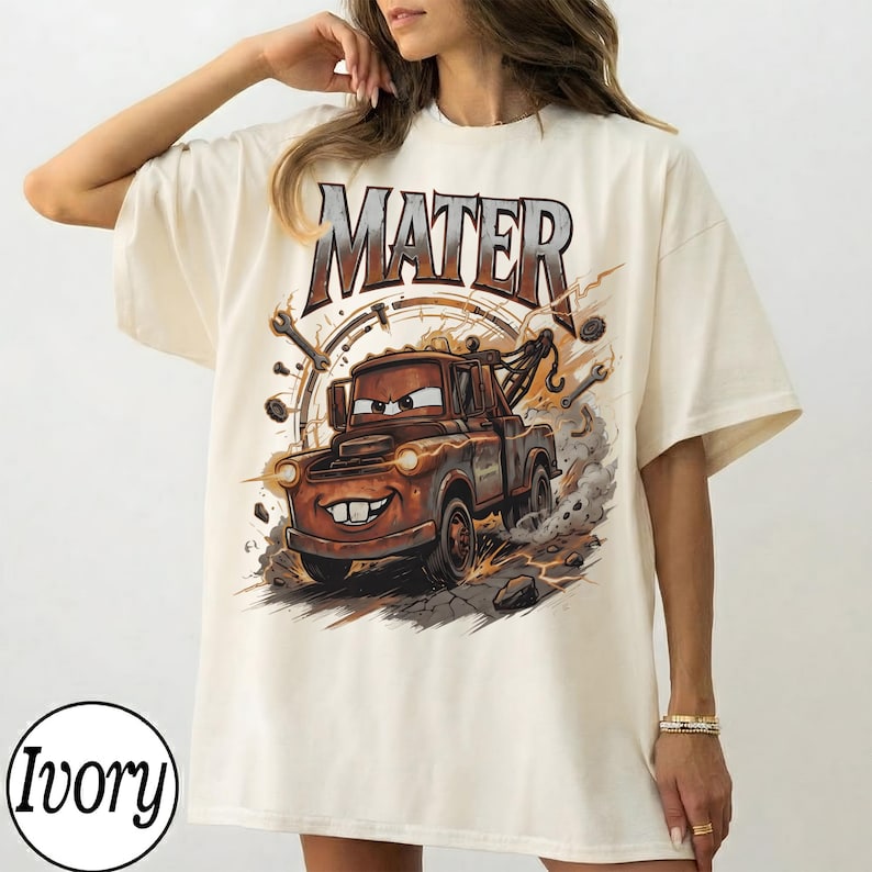 Puede incluir: Camiseta de color marfil con una imagen de dibujos animados de Mater de la pel&iacute;cula Cars. El gr&aacute;fico incluye la palabra "MATER" encima del personaje, con herramientas y un dise&ntilde;o de reloj en el fondo. La camiseta es de corte holgado.