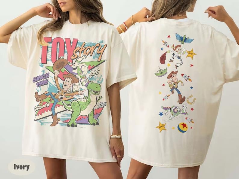 Puede incluir: Una camiseta color marfil con un gr&aacute;fico de Toy Story. El frente muestra a Woody, Rex y el texto "Toy Story Since 1995". La parte posterior presenta una disposici&oacute;n vertical de Woody, Buzz Lightyear, un alien&iacute;gena, un cohete, una pelota y estrellas.