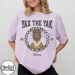 May include: A light purple t-shirt featuring the text "Yax the Yak" above a circular graphic of a yak meditating. The graphic includes the Disney logo and the numbers "20" and "16".