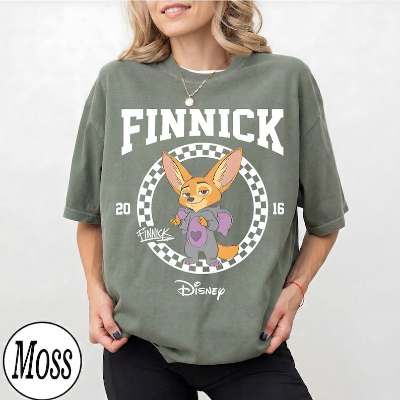 May include: Olive green t-shirt featuring a cartoon image of Finnick from Disney's Zootopia. The design includes the name "FINNICK" in white block letters, the year "2016", and the Disney logo. The shirt has a relaxed fit.