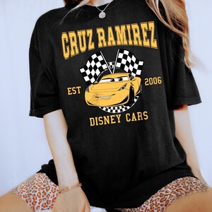 May include: A white ceramic mug with a black handle and the text "But First, Coffee" in a bold, black font. The mug is filled with a dark liquid, likely coffee, and sits on a light-colored surface.