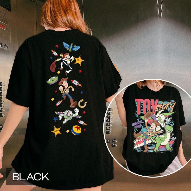 Puede incluir: Una camiseta negra con una disposici&oacute;n vertical de personajes de Toy Story, incluyendo a Woody, Buzz Lightyear y un alien&iacute;gena, junto con estrellas y cohetes. El recuadro frontal muestra el logo de Toy Story con Woody y Rex.