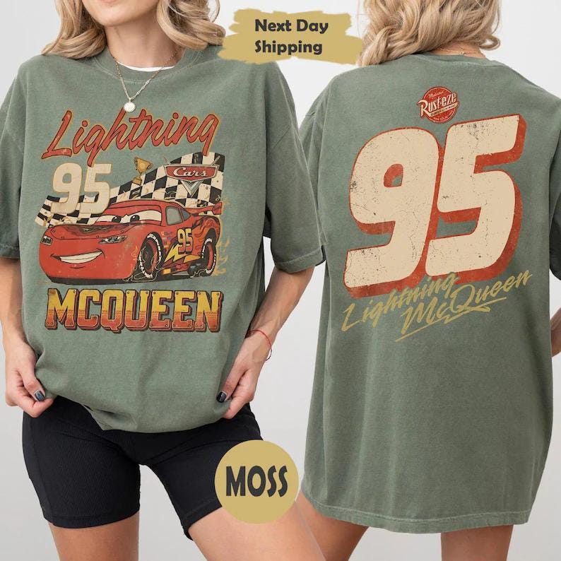May include: Green t-shirt with a distressed Lightning McQueen graphic from the Cars film. The front shows the number 95, "Lightning McQueen," and a chequered flag. The back features a large number 95 and the character's name in a vintage style.