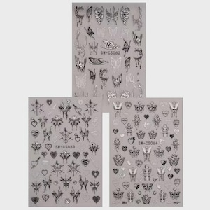 Könnte beinhalten: Drei Bögen Nagelkunst-Aufkleber mit Schmetterlings- und Herzmotiven in Schwarz und Silber. Die Bögen sind mit SW-CS062, SW-CS063 und SW-CS064 beschriftet. Die Aufkleber haben verschiedene Schmetterlingsflügelformen und Herzdesigns.