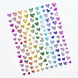 May include: A sheet of small adhesive nail decals featuring a variety of heart shapes in a rainbow color gradient. The hearts display diverse patterns including stripes, dots, and solid fills. The text LC427 is printed in the center of the sheet.