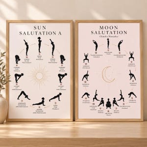 May include: Two framed posters with light backgrounds and wooden frames. The left poster displays Sun Salutation A with black silhouettes of yoga poses arranged in a circle around a sun icon. The right poster shows Moon Salutation with black silhouettes of yoga poses arranged in a circle around a moon icon.