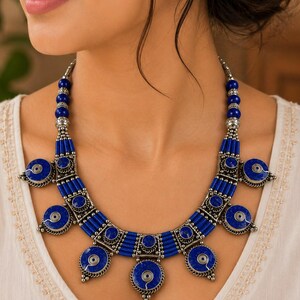 May include: A statement necklace featuring deep blue lapis lazuli beads and circular silver-toned metal accents. The design includes multiple cylindrical blue beads arranged in segments, interspersed with ornate silver-toned metal spacers and charms.