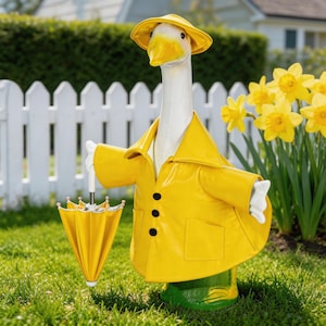 Puede incluir: Una estatua de jardín caprichosa de un ganso con un impermeable y sombrero amarillos, sosteniendo un paraguas a juego. El ganso está sobre botas verdes, con una valla blanca y narcisos amarillos.