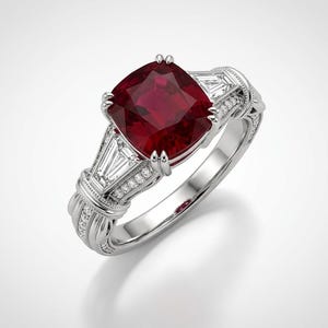 Puede incluir: Un anillo de tono plateado con una gran piedra preciosa de color rojo intenso en talla cojín en el centro. La banda está acentuada con dos piedras claras en talla baguette a cada lado, flanqueadas por filas de pequeñas piedras claras.