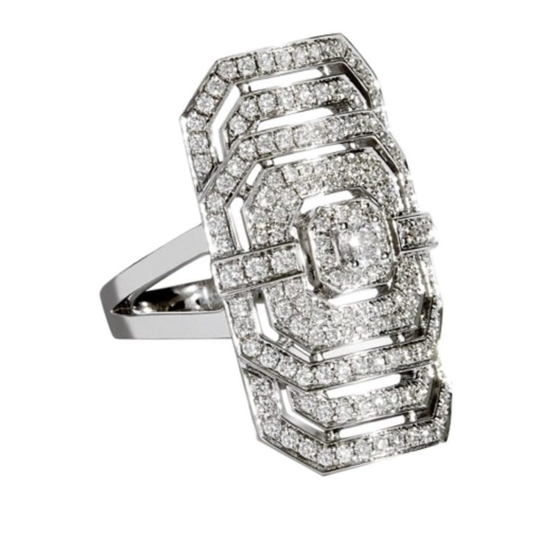 May include: A silver ring with a rectangular, geometric design. The ring is encrusted with numerous small, sparkling diamonds, creating a dazzling effect. The ring's band is a simple, polished silver.