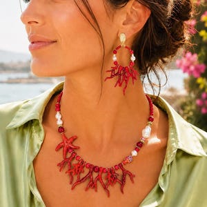 May include: A necklace and matching drop earrings set featuring red coral-shaped branches, small red beads, and white pearls. The necklace includes a red starfish charm and a small multicolored bead, while the earrings feature a circular gold-tone stud.