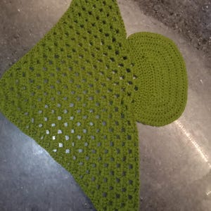 Puede incluir: Un accesorio de ganchillo color verde lima que presenta una gran sección triangular con un patrón calado de tipo granny square y una pieza circular más pequeña y sólida unida a un lado, elaborada con hilo de textura uniforme.