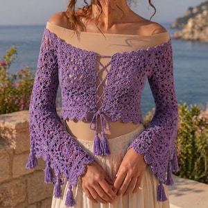May include: A purple, off-the-shoulder crochet top with long bell sleeves. The top features a lace-up front and is adorned with tassels at the sleeves and waist. The crochet design has a floral pattern.