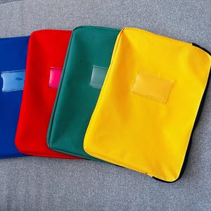 May include: Four rectangular document pouches in blue, red, green, and yellow. Each pouch features a smooth, solid-colored exterior with a clear, rectangular plastic label window centered on the front. The pouches are arranged in a side-by-side row.