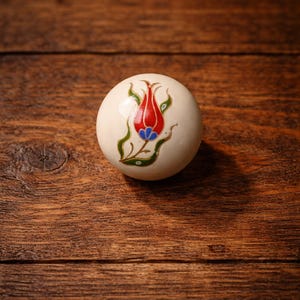 May include: A trio of cream-glazed ceramic mugs with a speckled finish. Each mug is adorned with a hand-painted design: a blue and green leaf, a yellow flower, and a red berry. The mugs have a simple, modern design.