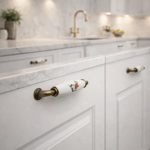 May include: White kitchen cabinets with decorative ceramic and brass hardware. The cabinet pulls feature a white ceramic handle with a floral design and brass accents. The kitchen has a marble countertop and a gold faucet.