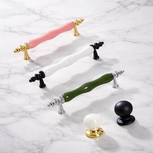May include: Cabinet hardware set featuring three different colored handles: pink with gold accents, white with black accents, and green with silver accents. Also included are a black knob and a white knob with gold accents.