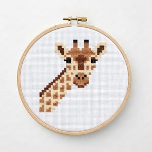 May include: A cross-stitch embroidery of a giraffe's head and neck, featuring shades of brown and tan against a white background. The artwork is displayed in a round wooden embroidery hoop, perfect for home decor.