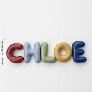 Op de afbeelding: Een decoratieve naam met de naam "CHLOE" in bubbelletters. De letters zijn ongeveer 11 cm hoog en zijn in tinten rood, blauw, groen, geel en marine. Ideaal voor een kinderkamer.