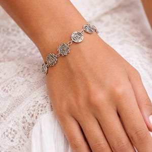 May include: A silver bracelet featuring circular charms with intricate designs. The bracelet is worn on a wrist, with the charms linked together. The bracelet is a piece of jewelry.