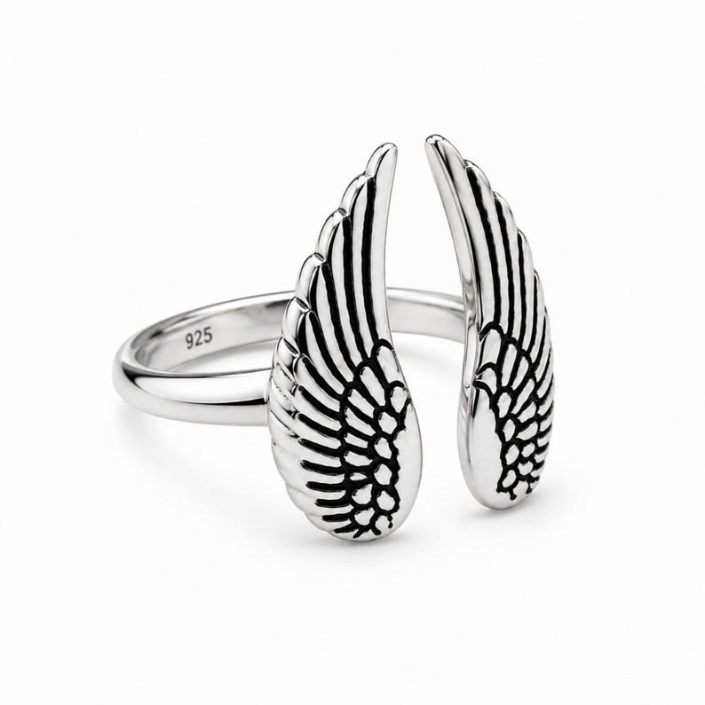 May include: A silver ring featuring an open wing design. The ring has two detailed wings, each with intricate feather detailing. The band is smooth and has the number "925" stamped on it. The ring is set against a white background.