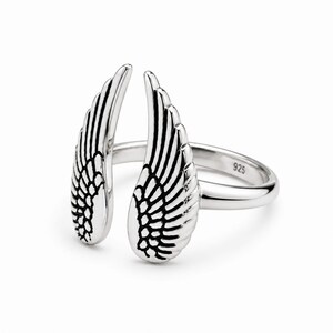 May include: A silver ring with an open design featuring two detailed wing shapes. The ring is made of polished metal and has the number "925" stamped on the band. The wings are positioned to appear as if they are wrapping around a finger.