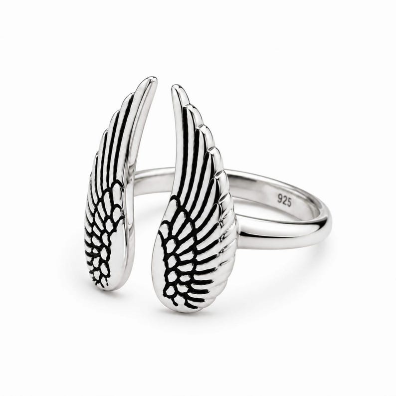 May include: A silver ring with an open design featuring two detailed wing shapes. The ring is made of polished metal and has the number "925" stamped on the band. The wings are positioned to appear as if they are wrapping around a finger.