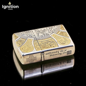 May include: A silver and gold-toned metal lighter with intricate engraved designs. The lighter features a cross on the side and the text "Our Horsemen of the Apocalypse". The top has a detailed illustration. The brand "Ignition House" is in the top left corner.