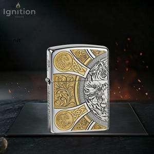 May include: A silver and gold-toned metal lighter with intricate engraved designs. The lighter features a detailed pattern with Celtic knotwork and a central illustration. The text "Ignition House" is visible in the upper left corner.