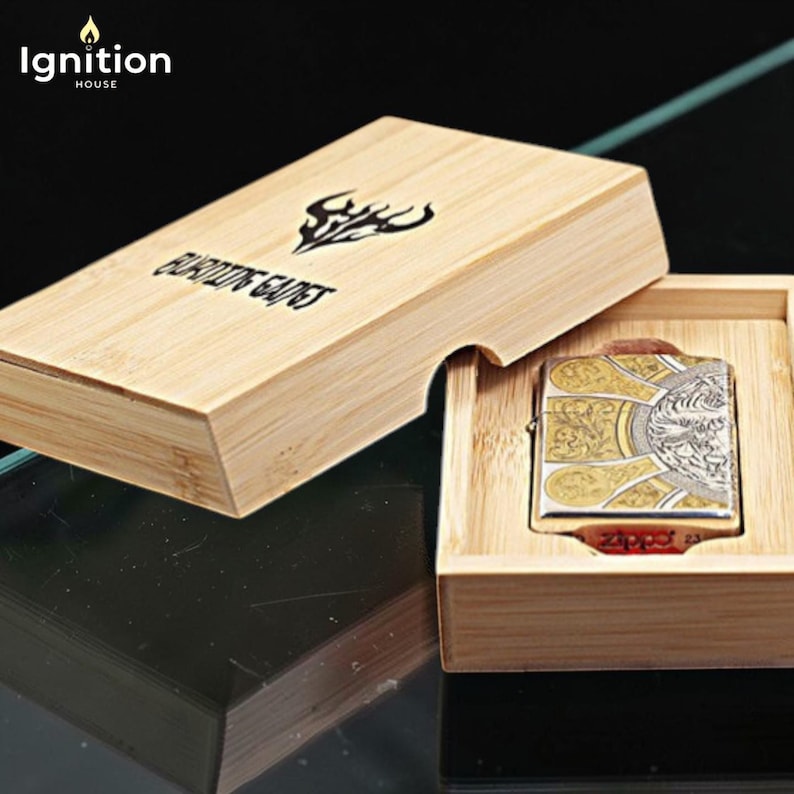 May include: A decorative lighter with a gold and silver design, presented in a wooden box. The lighter features an ornate pattern and a detailed image. The box is made of light-colored wood and has the text "BURNING GAINS".