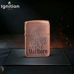 May include: A copper-colored lighter with a cowboy and horse design, and the word "Marlboro" in a serif font. The lighter has the text "Ignition House" at the top left.
