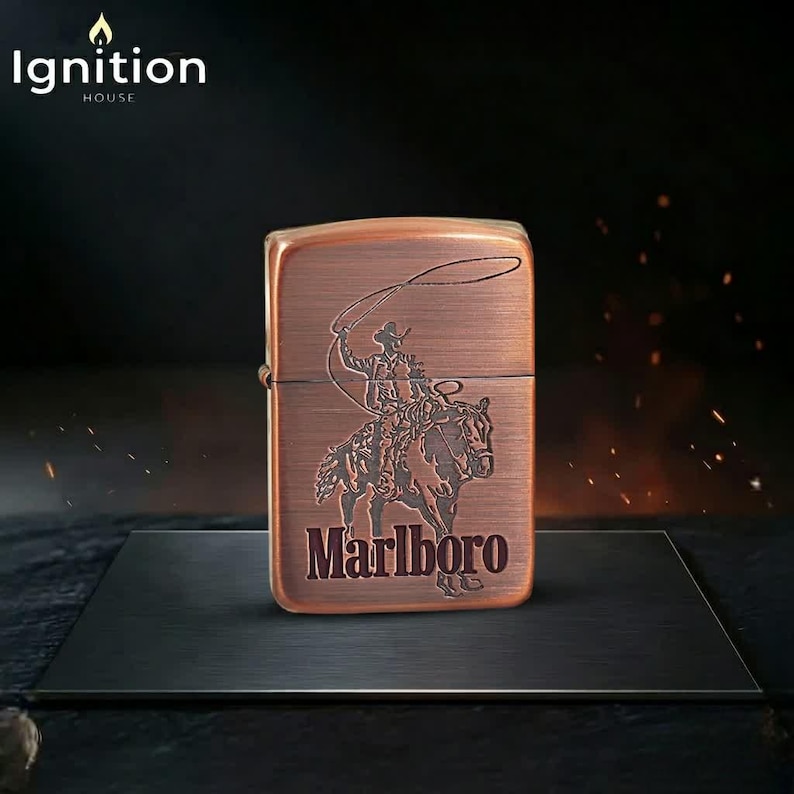 May include: A copper-colored lighter with a cowboy and horse design, and the word "Marlboro" in a serif font. The lighter has the text "Ignition House" at the top left.