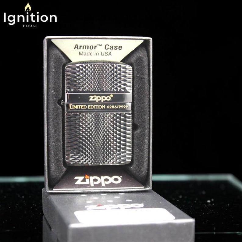 May include: A silver Zippo lighter with a diamond pattern, presented in a black box. The lighter is a limited edition, marked 6286/9999, and is an Armor Case, made in the USA. The Zippo logo is visible on the lighter and the box.