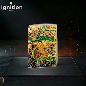 May include: A decorative metal lighter with a detailed dragon design in gold, green, and red. The lighter features the text "Ignition House" in white. The dragon is set against a backdrop of green mountains and a cream-colored sky.